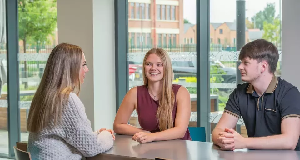 Three colleagues having a conversation around a table in a modern office.