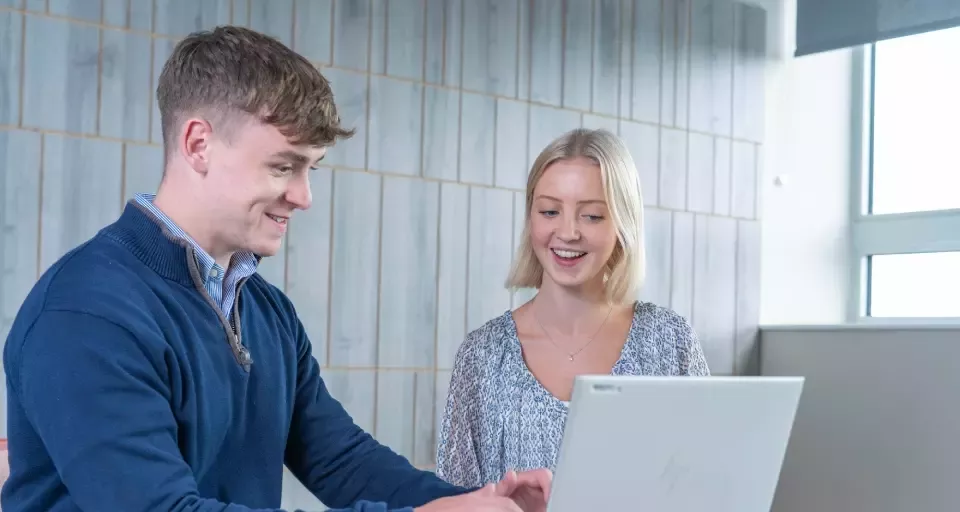 Two people working together on a laptop in an office.