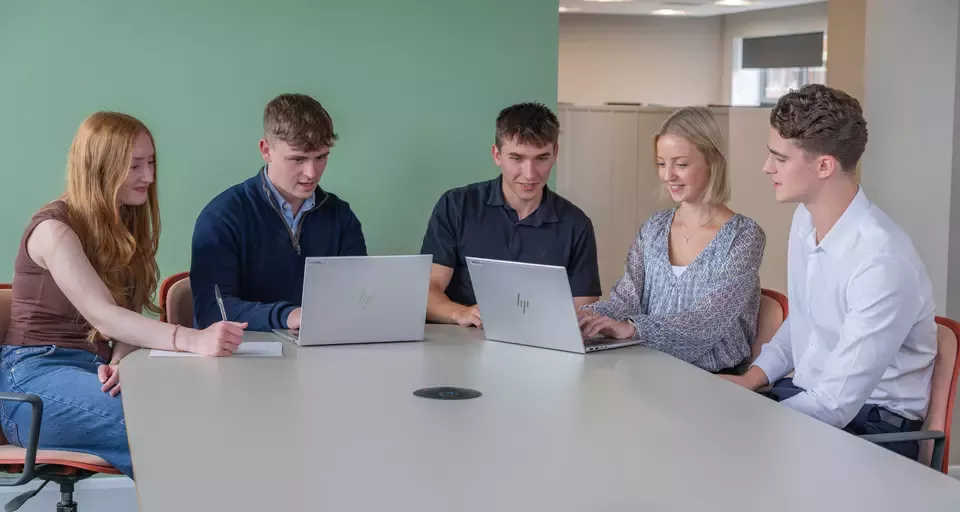 Five colleagues working together around a table with laptops.