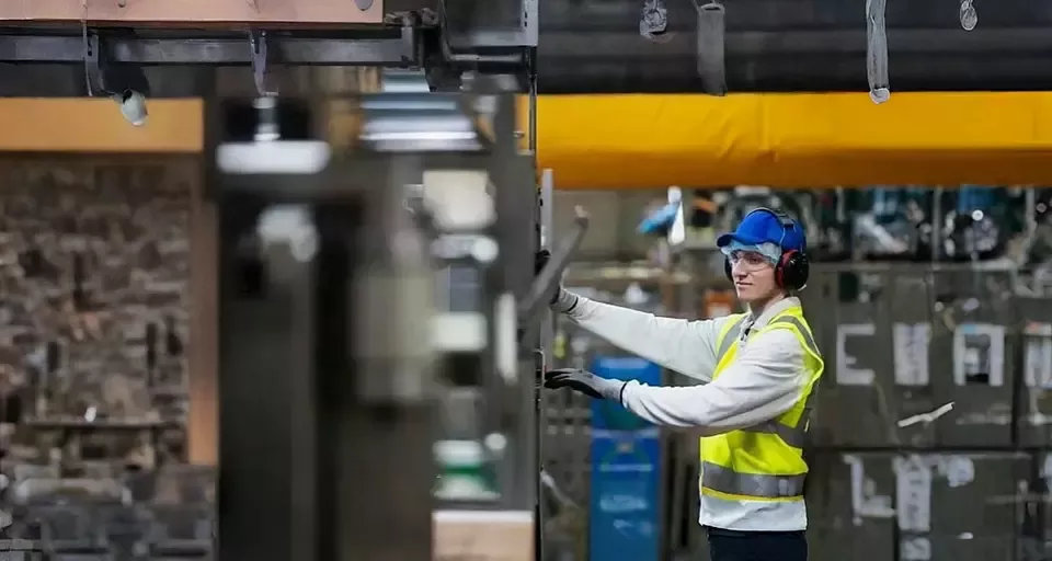 Worker operating machinery in a factory while wearing safety equipment.