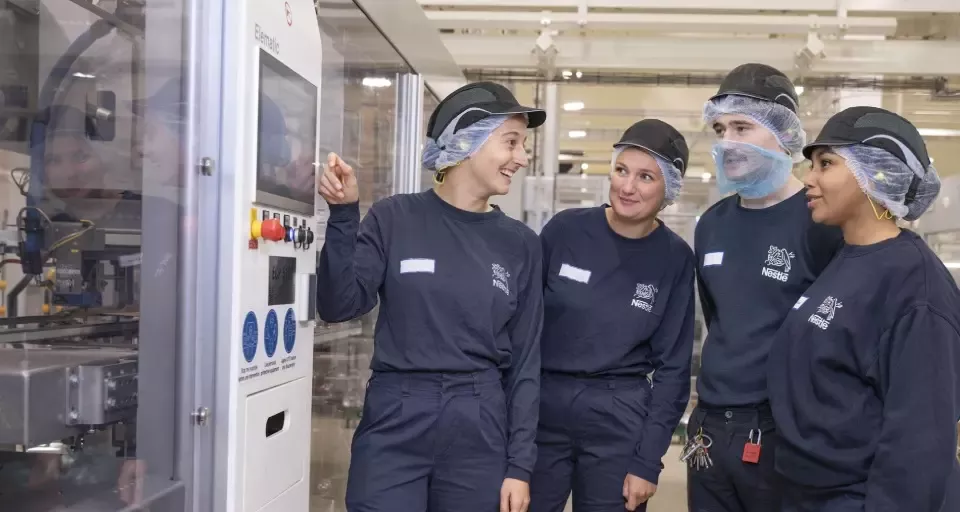 Four people standing beside machinery in a production facility