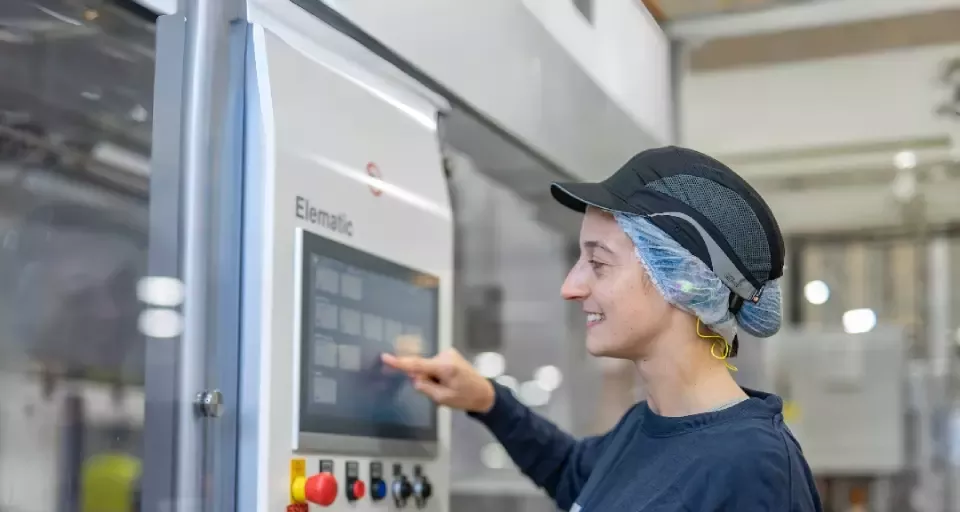 Apprentice operating a touchscreen control panel on manufacturing equipment in a food production facility while wearing work