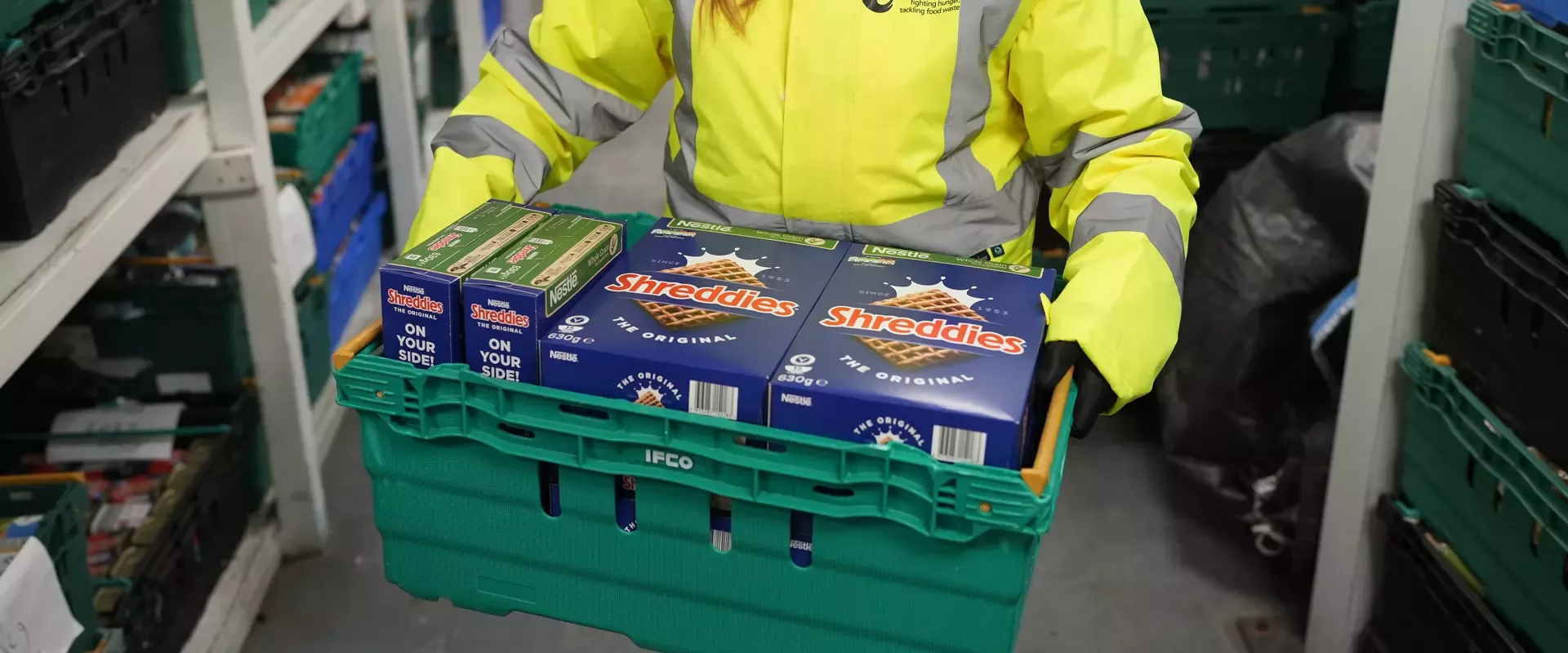 Person holiding green plastic crate containing boxes of Shreddies