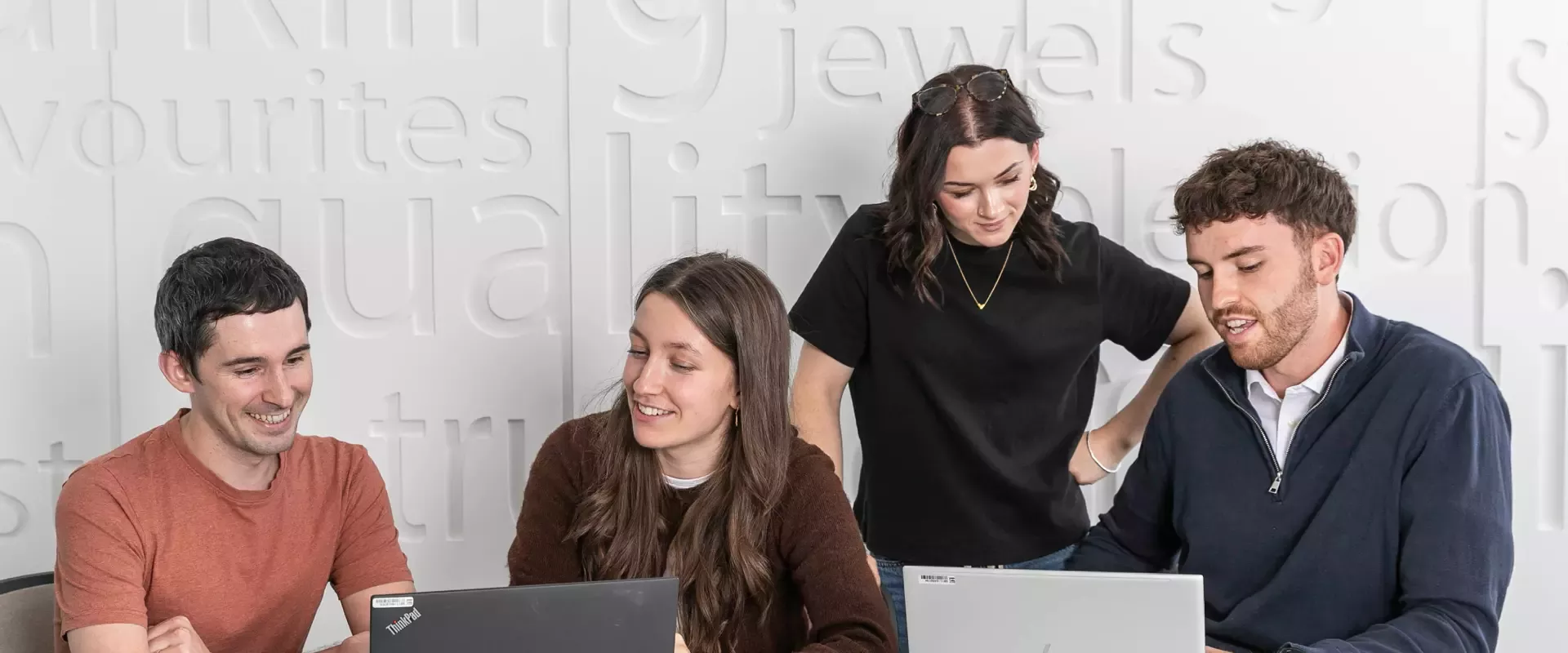 Four colleagues working together at a table with laptops.