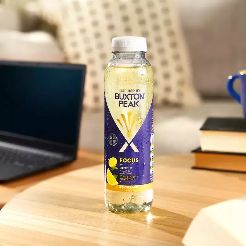 Bottle of water sitting on a desk next to a laptop.
