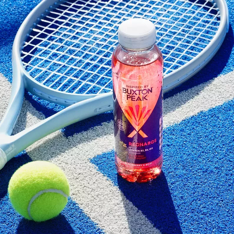 Bottle of water sitting on tennis court next to a racket and ball.