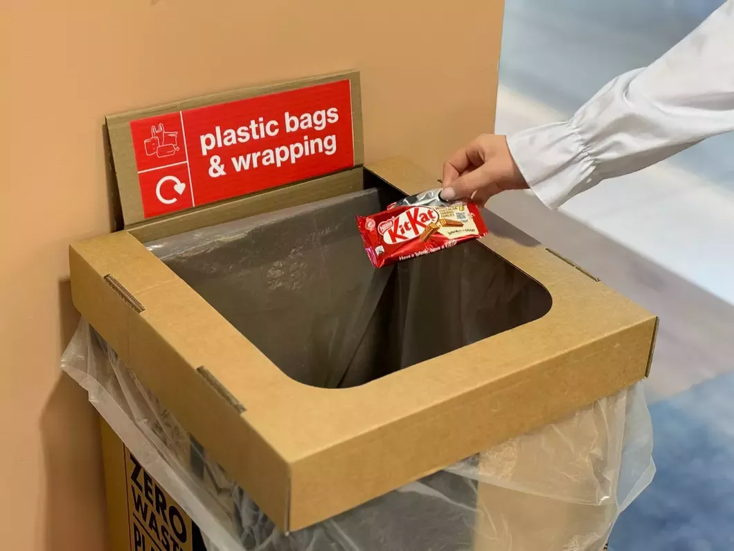 Hand holding packaging over a recycling bin.