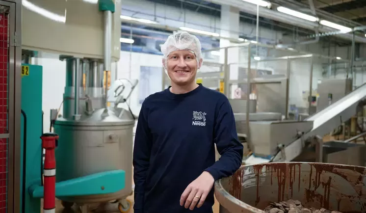 Man leaning on a bucket of chocolate pieces inside a factory