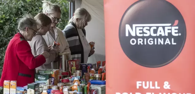 An image of four white women handing out Nestlé products at a stall, next to a Nescafé Original sign.