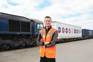 A man standing in front of rail freights, one of which advertises Nestlé's brand logos.
