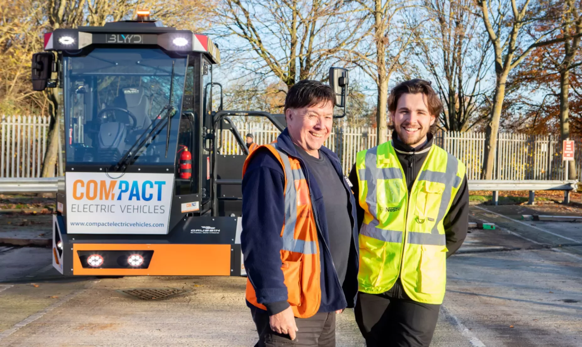 Two Nestlé colleagues stand in front of an electric shunter which is being trialled on the York site