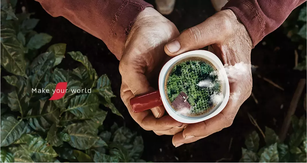 A cup of coffee in someone's hands, inside the cup is a farm landscape