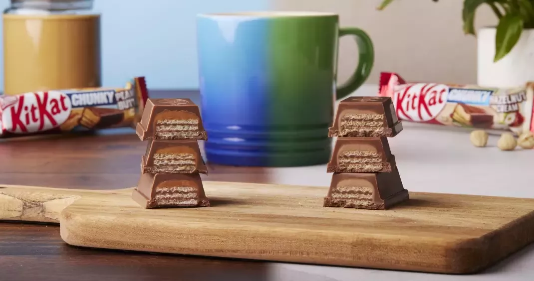 KitKat Chunky Peanut Butter sits on a chopping board, cut in half, next to KitKat Chunky Hazelnnut