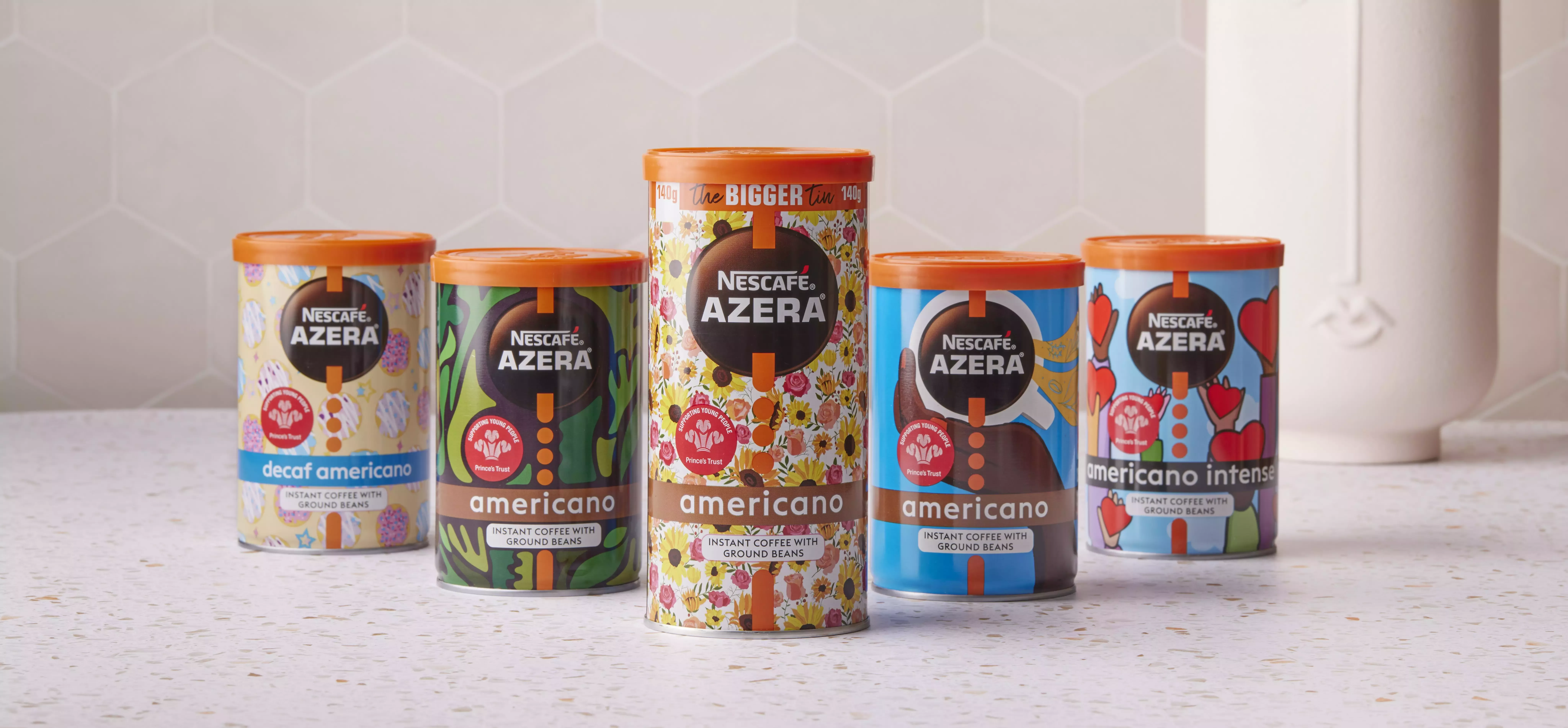 Five Nescafé Azera coffee tins, designed with bright colours and artistic designs, lined up on a cream counter top.