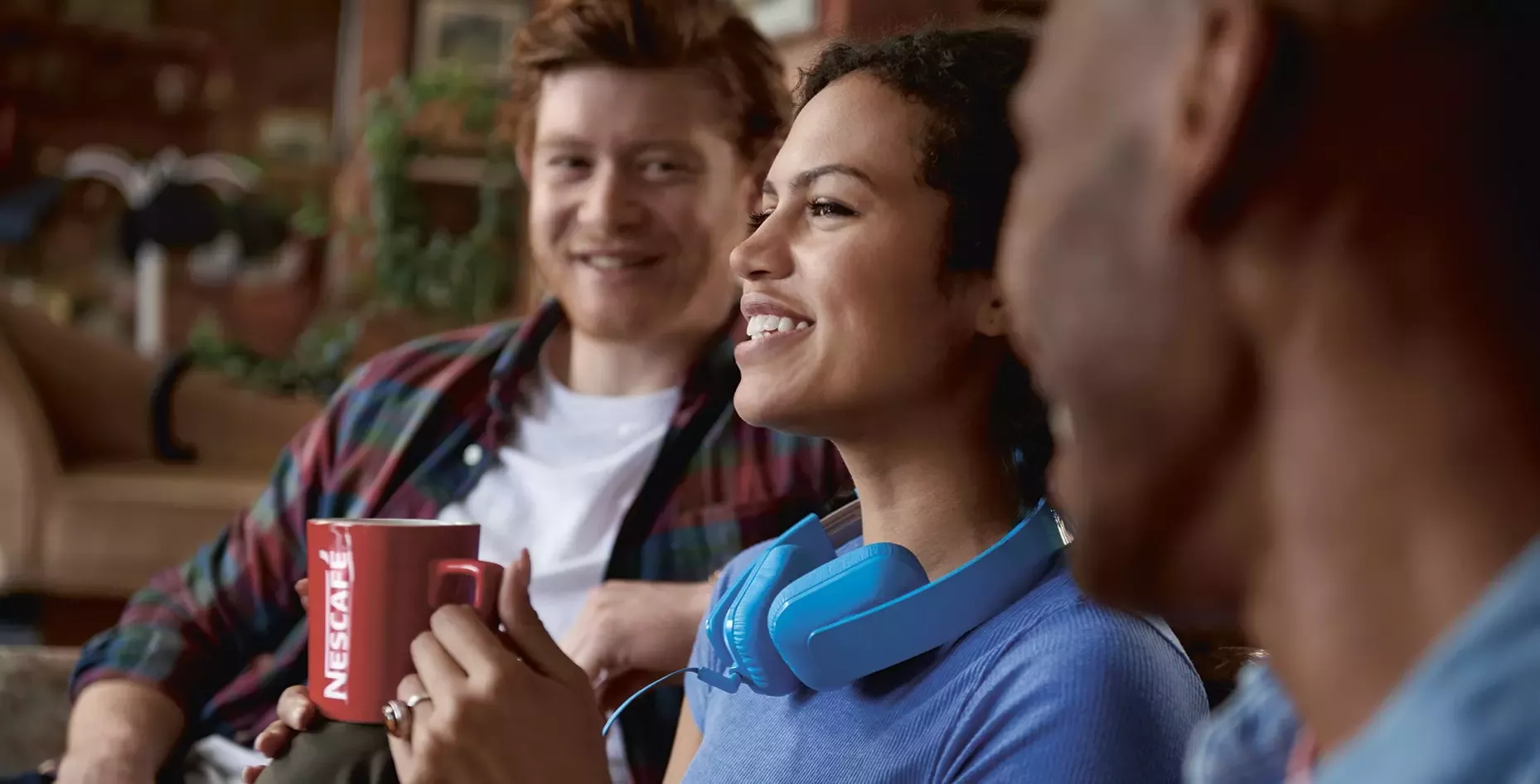 One man, one woman, and another man sitting down smiling. The woman is holding a red Nescafé coffee mug.
