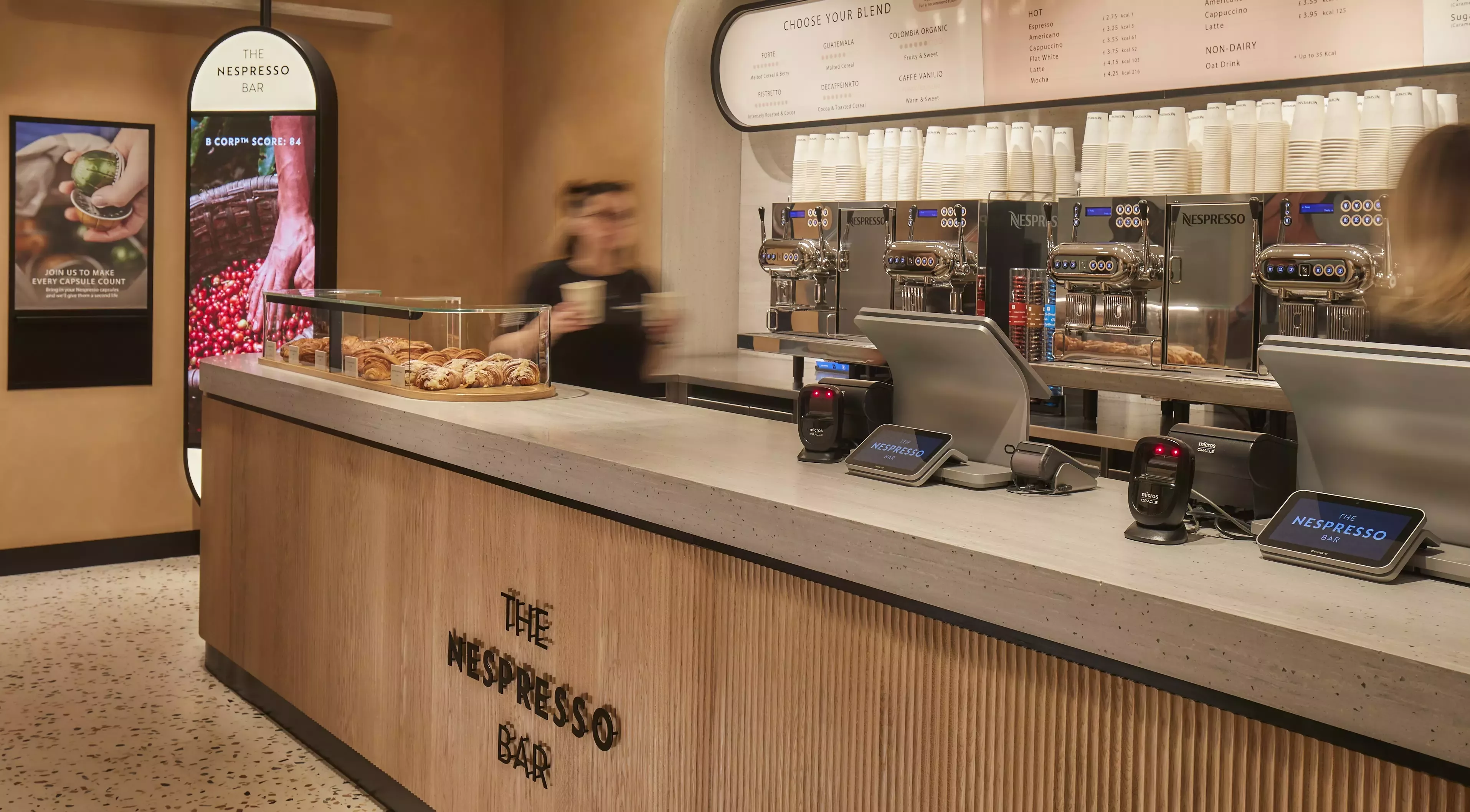 A wooden brown cafe bar with coffee machines and pastries on the counter top.