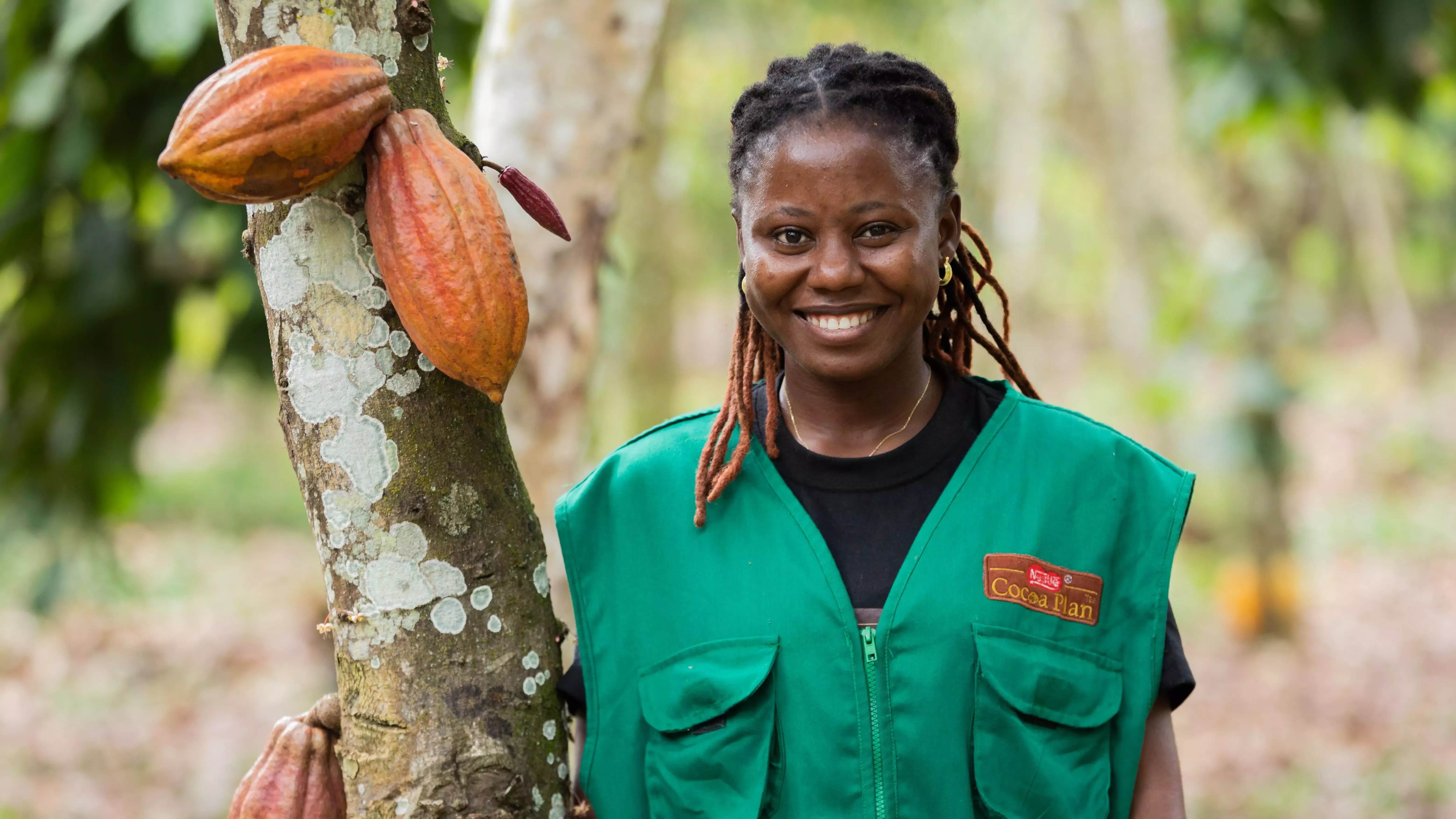 oman wearing green standing next to a cocoa pod tree.