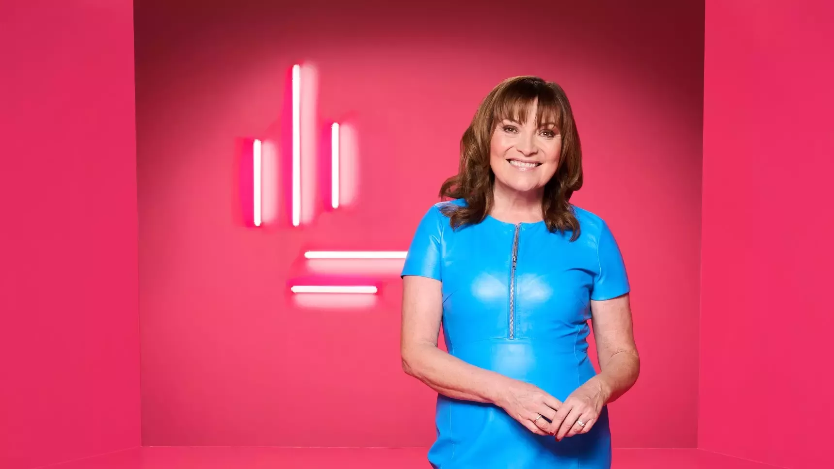 TV Presenter Lorraine Kelly stands in front of pink background