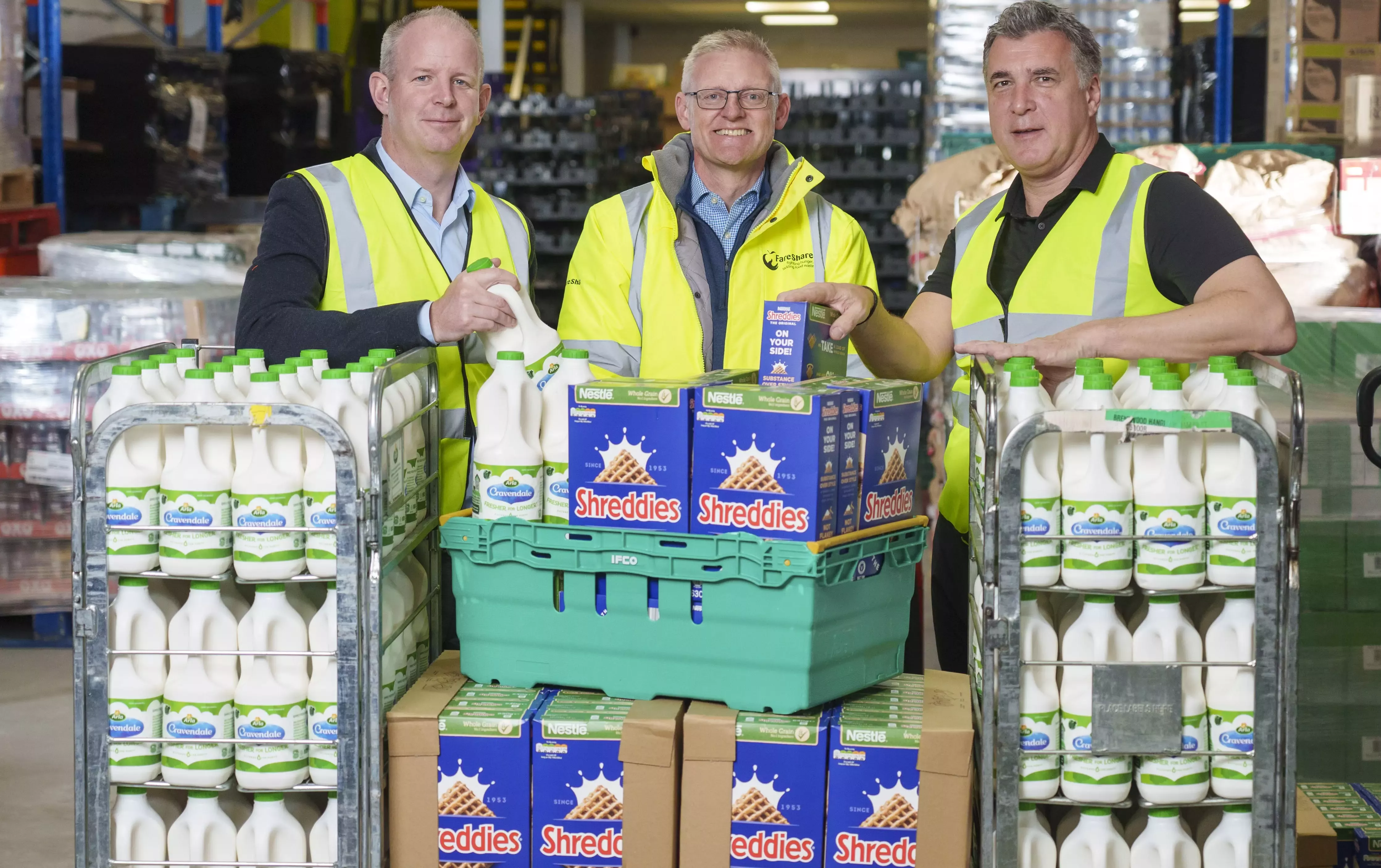 Nestlé and Arla team holding a bottle of Cravendale milk and a box of Shreddies cereal in a warehouse.