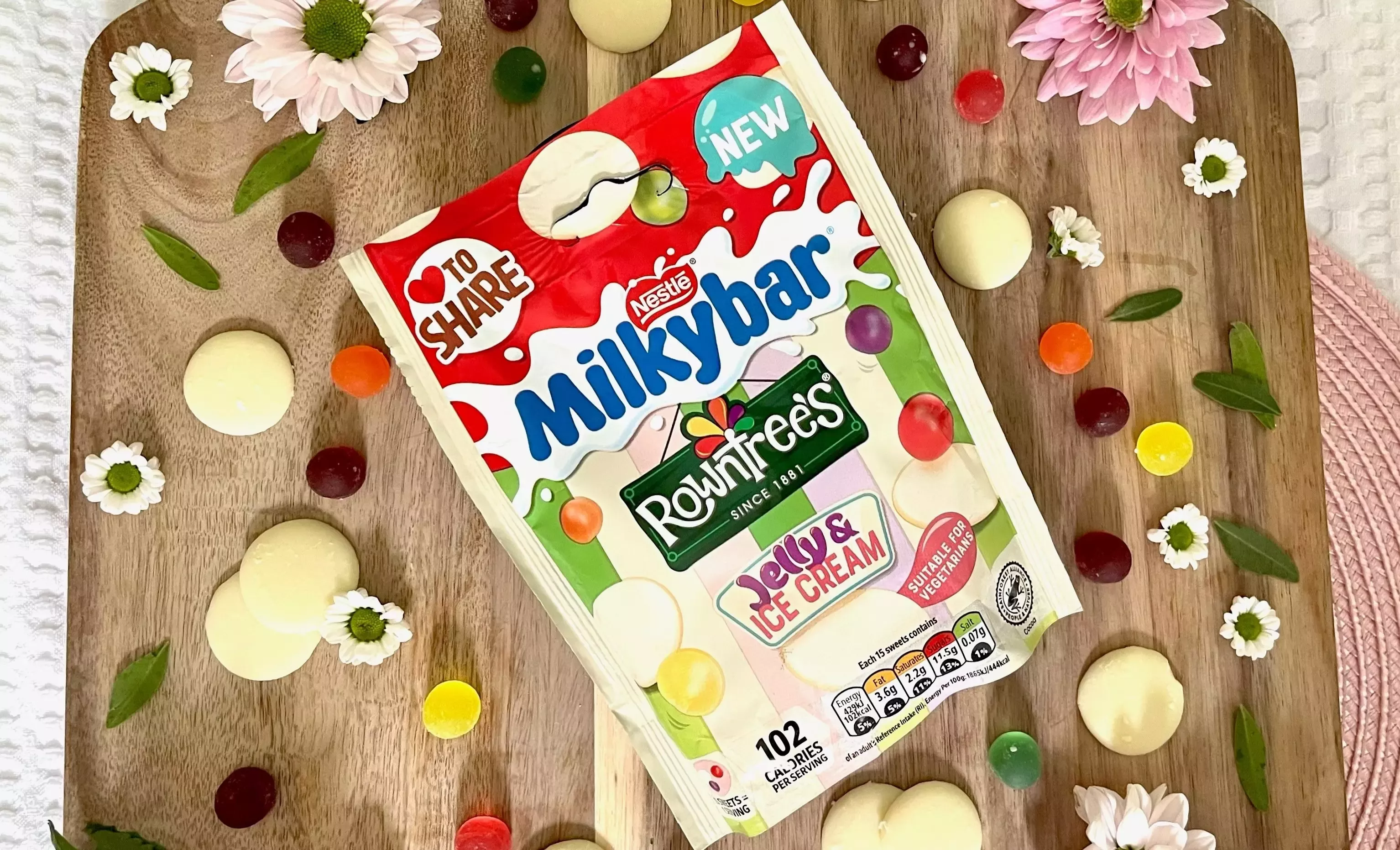A packet of Milkybar Jelly &amp; Ice Cream confectionery against a wooden chopping board background with floral features.