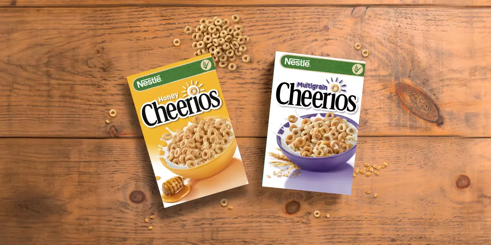 A landscape image of a golden box of Honey Cheerios and a white box of Multigrain Cheerios, on a dark wooden table.