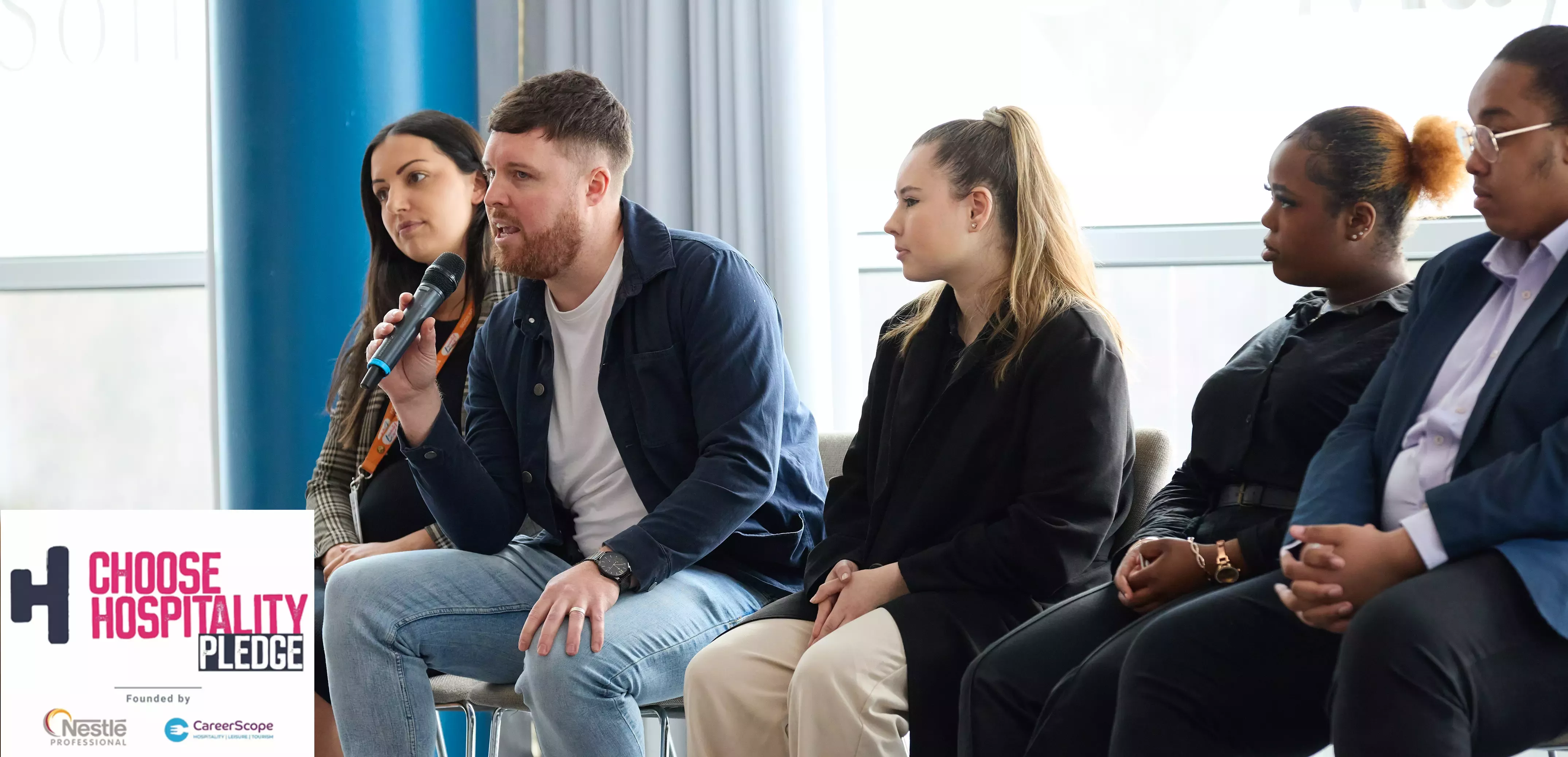 An image of a mixed gender group of hospitality workers sat on chairs talking together.