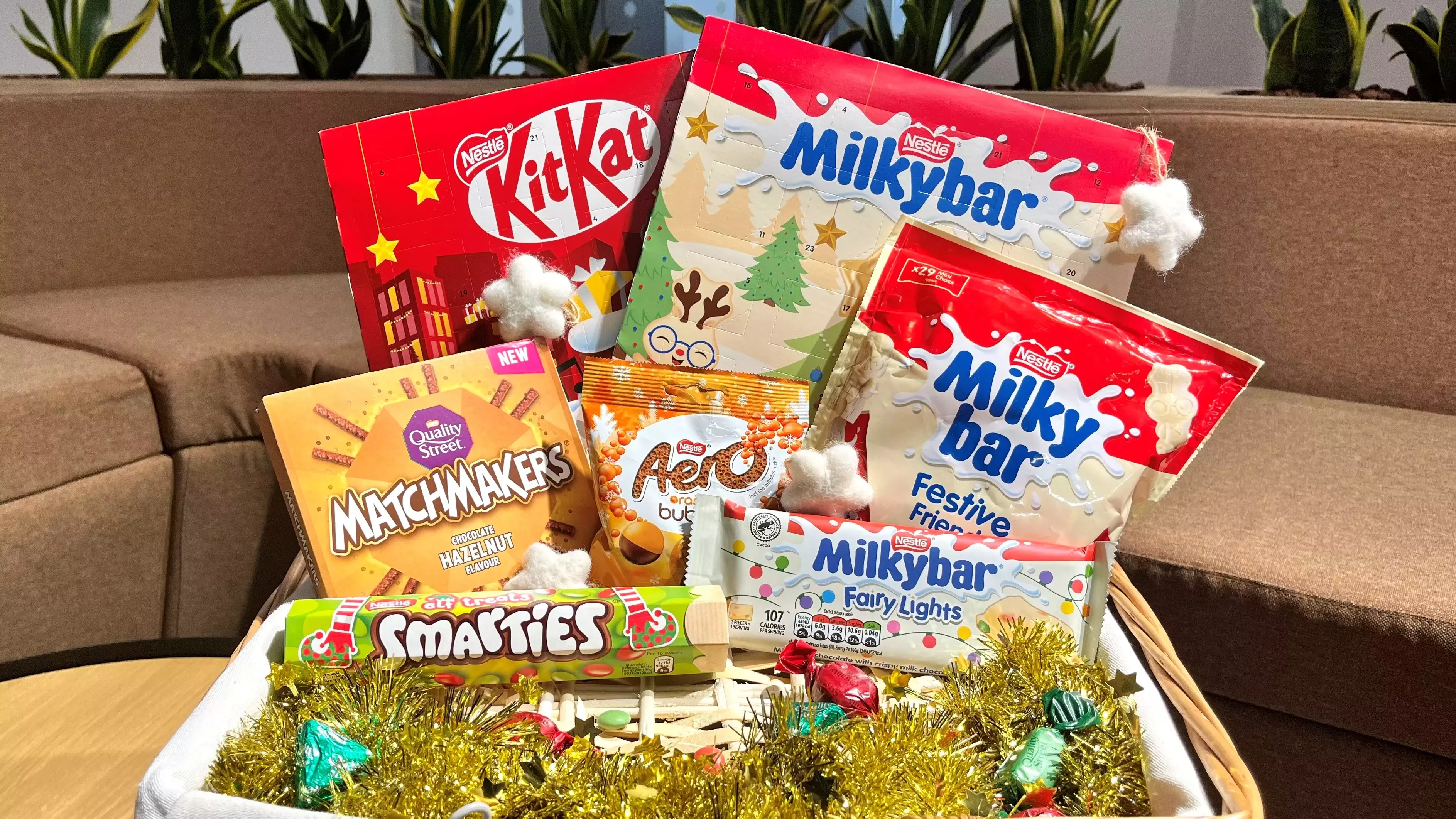 An image of Nestlé Christmas Confectionery including KitKat, Aero, Milkybar, Smarties & Matchmakers in a basket with tinsel. 