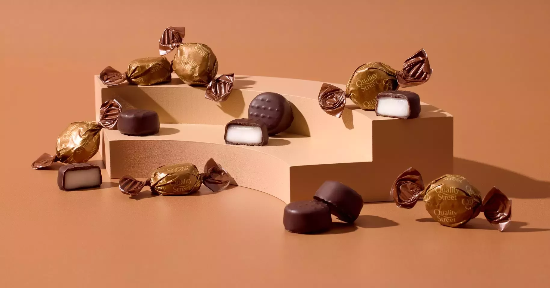 A selection of coffee creme sweets wrapped in a golden brown twist wrap next to unwrapped coffee creme with a white centre.