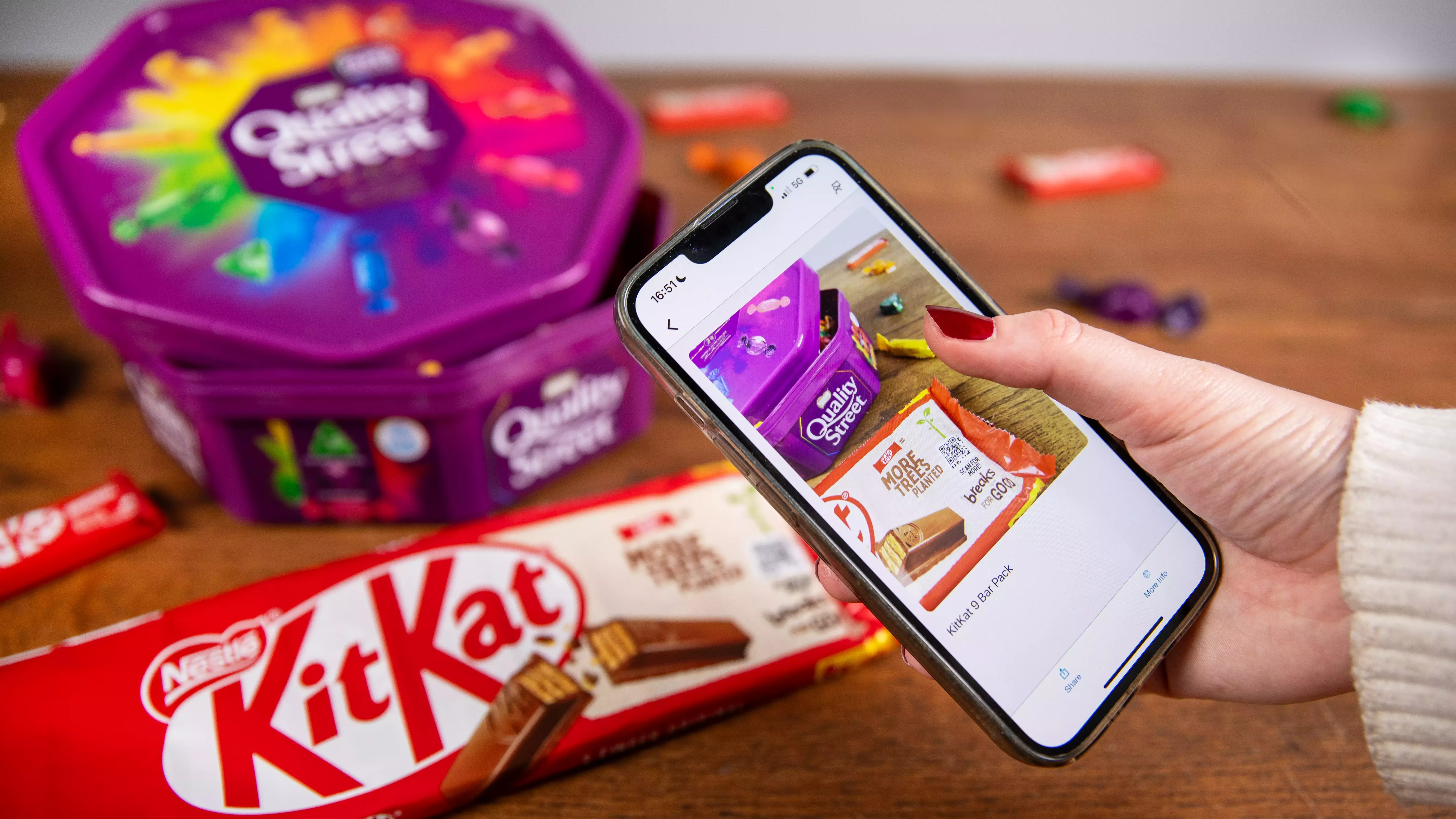 a close up of a woman’s hand holding a mobile phone, using the Seeing AI app to scan the new QR code on a KitKat multipack