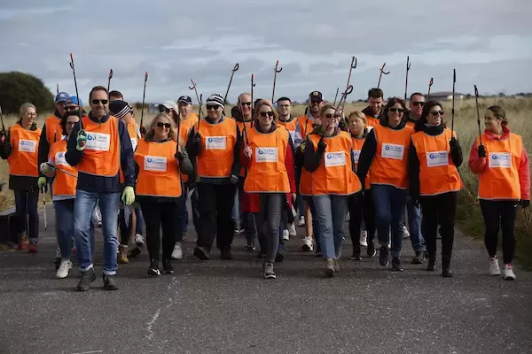 Group of 40 people wearing high vis vests and carrying litter pickers at the beach.