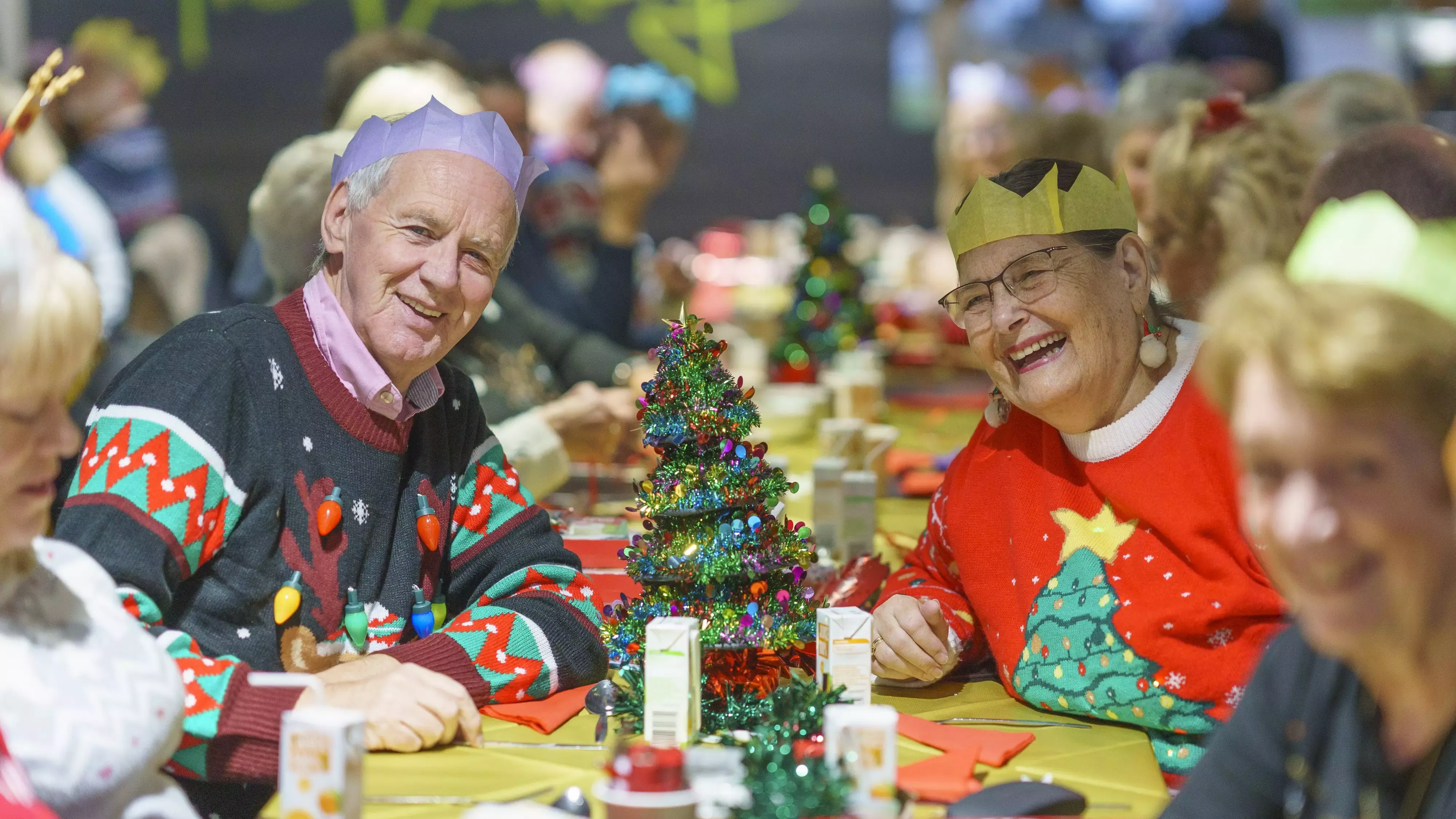 An elderly woman and an elderly man sitting at a Christmas lunch table. 