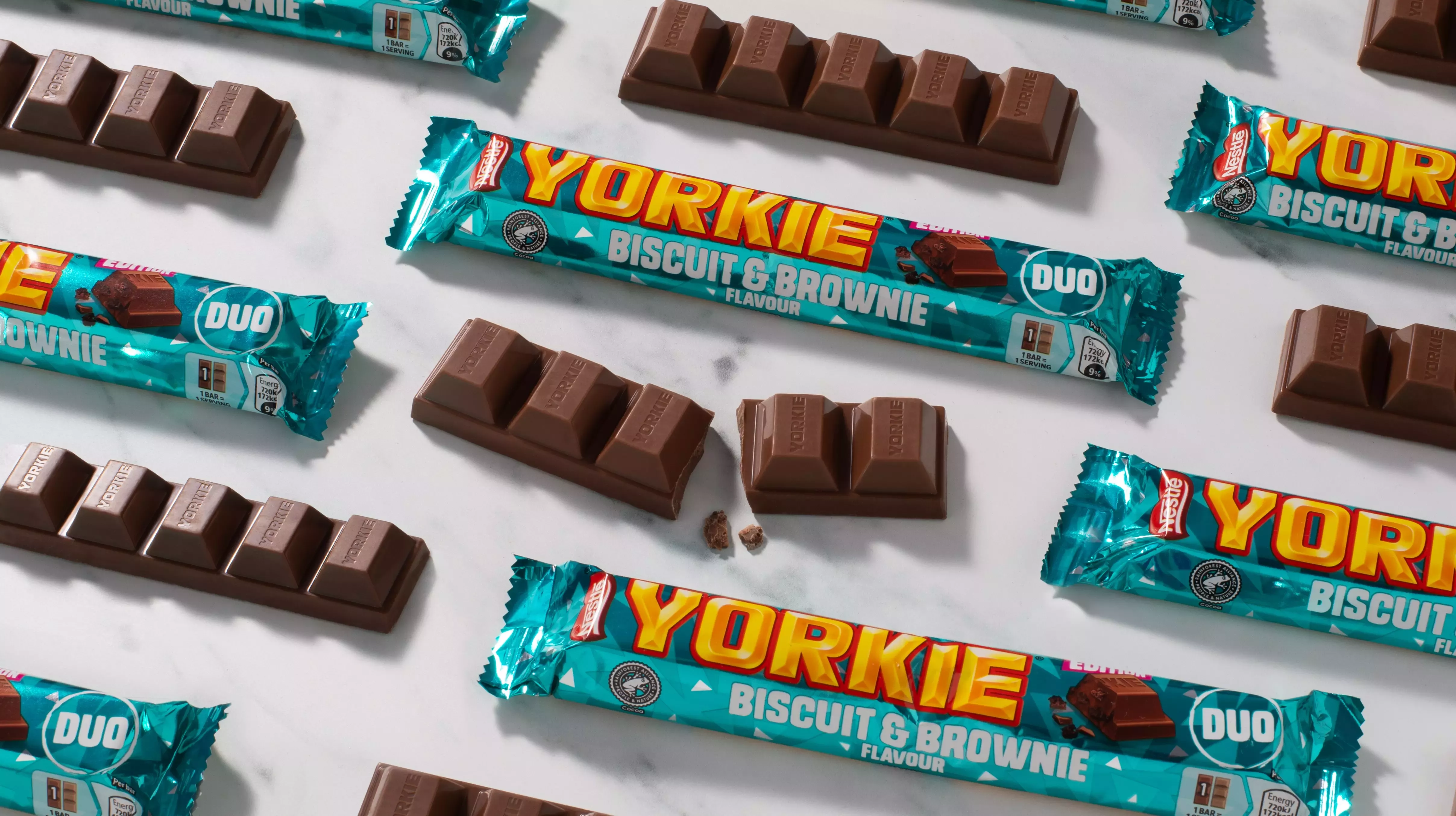 A landscape image of multiple Yorkie Biscuit &amp; Brownie flavour bars, wrapped in shiny teal packaging, some bars are open.