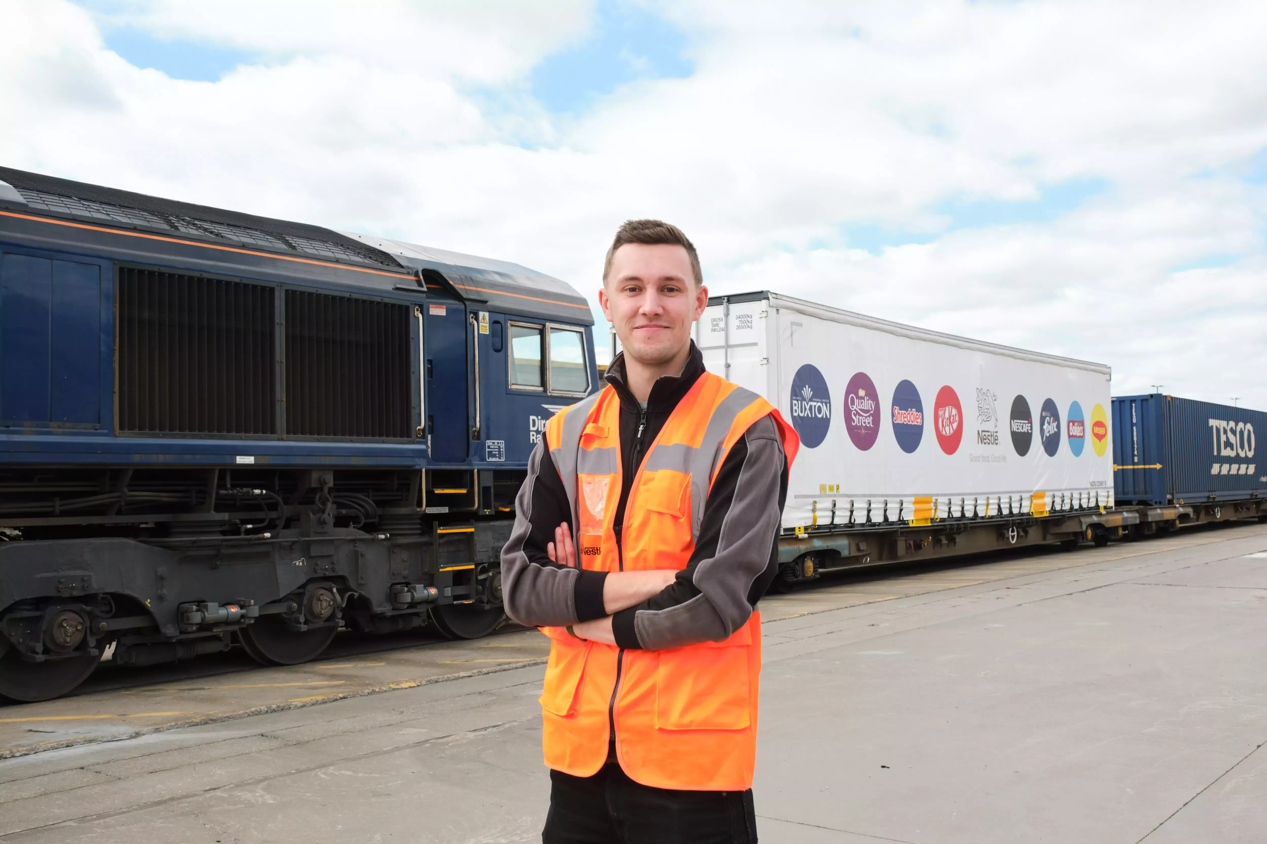 A man standing in front of rail freights, one of which advertises Nestlé's brand logos.