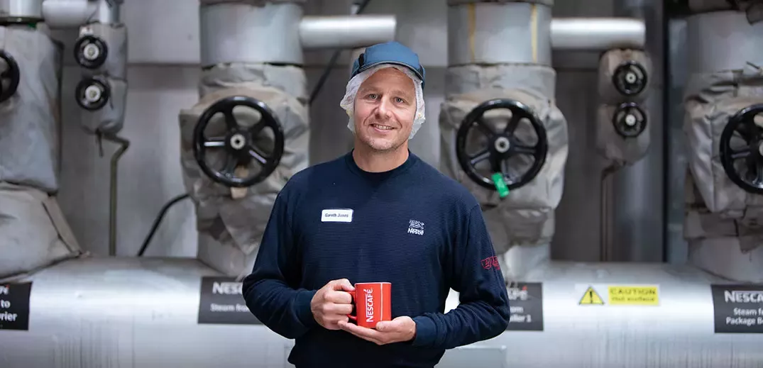 Man in a factory environment holding a Nescafé mug