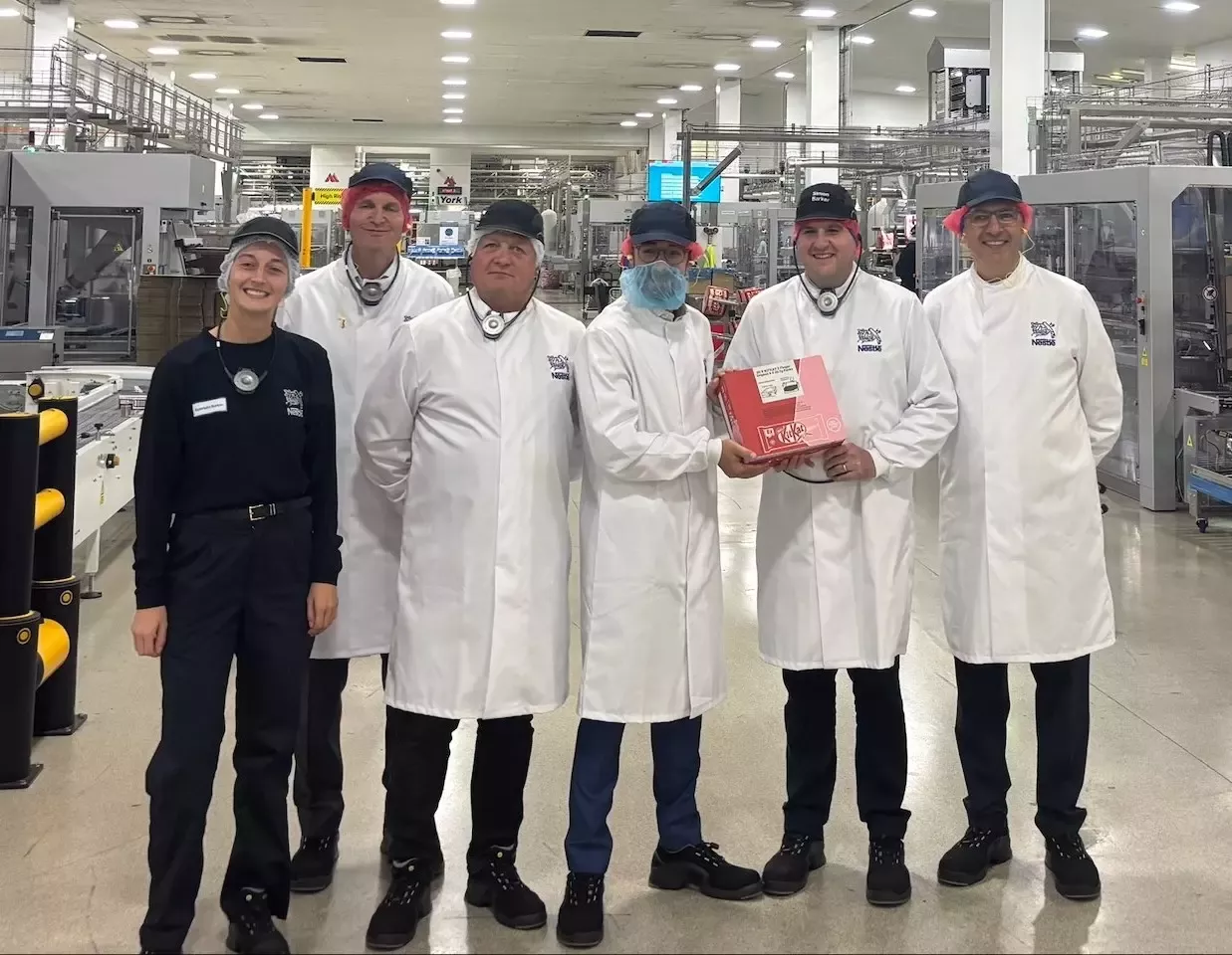 Luke Charters MP (centre) stood inside Nestlé York's KitKat factory, next to Nestlé employees, smiling.