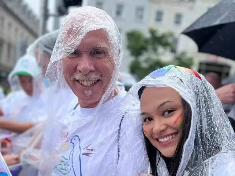 A man and a woman wearing rain ponchos whilst at a Pride march.