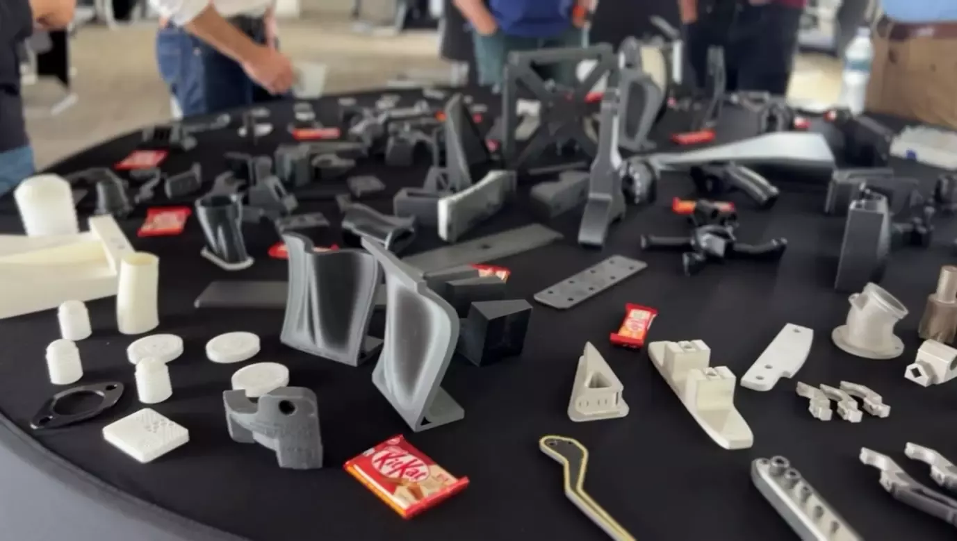 A landscape image of a black table with a variety of 3D printed machinery parts on it. KitKat bars are also seen on the table