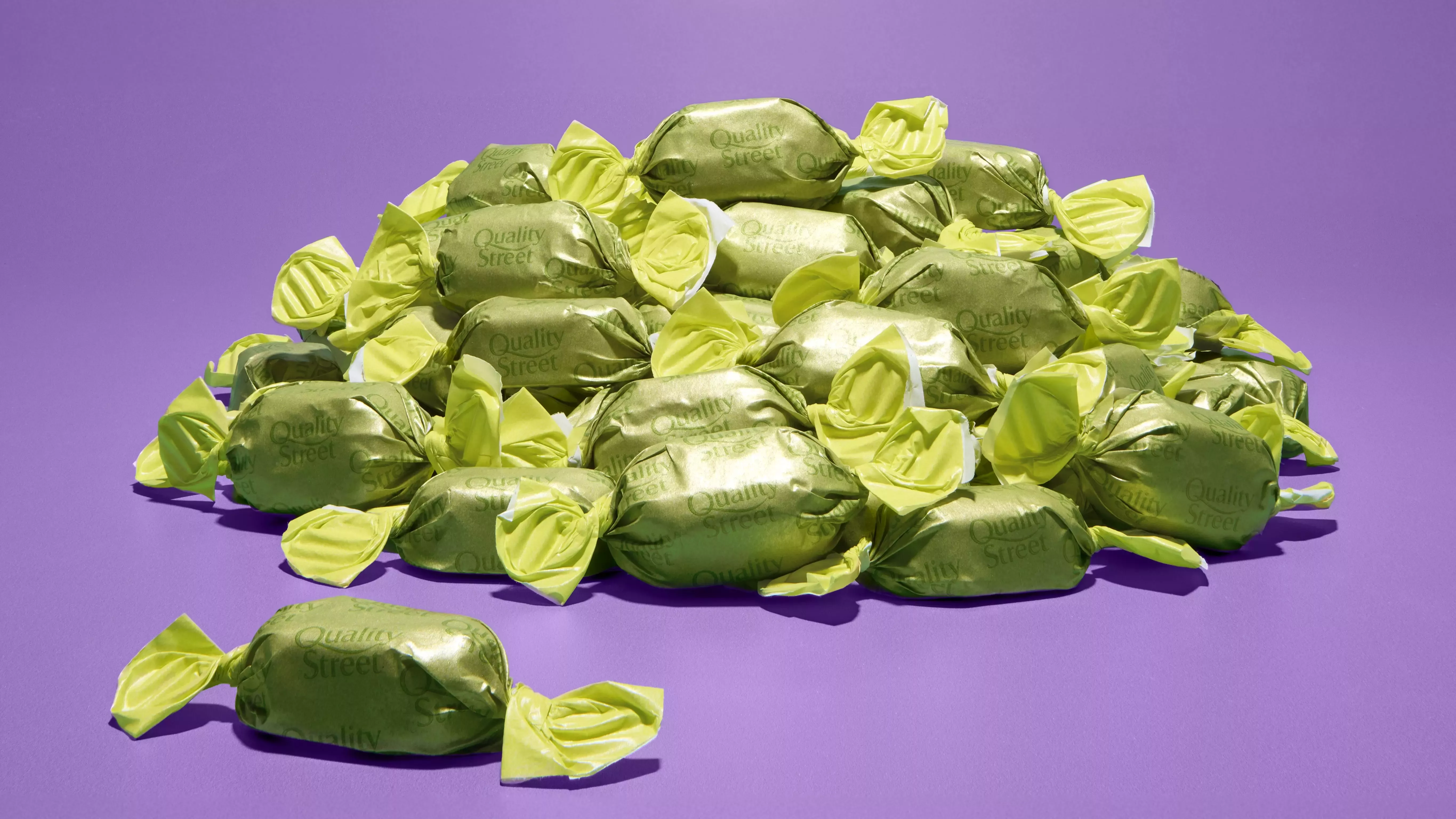 Quality Street mystery sweet wrapped in a green wrapper in front of a purple background