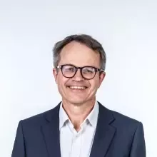 Man wearing glasses and a suit with a grey background.