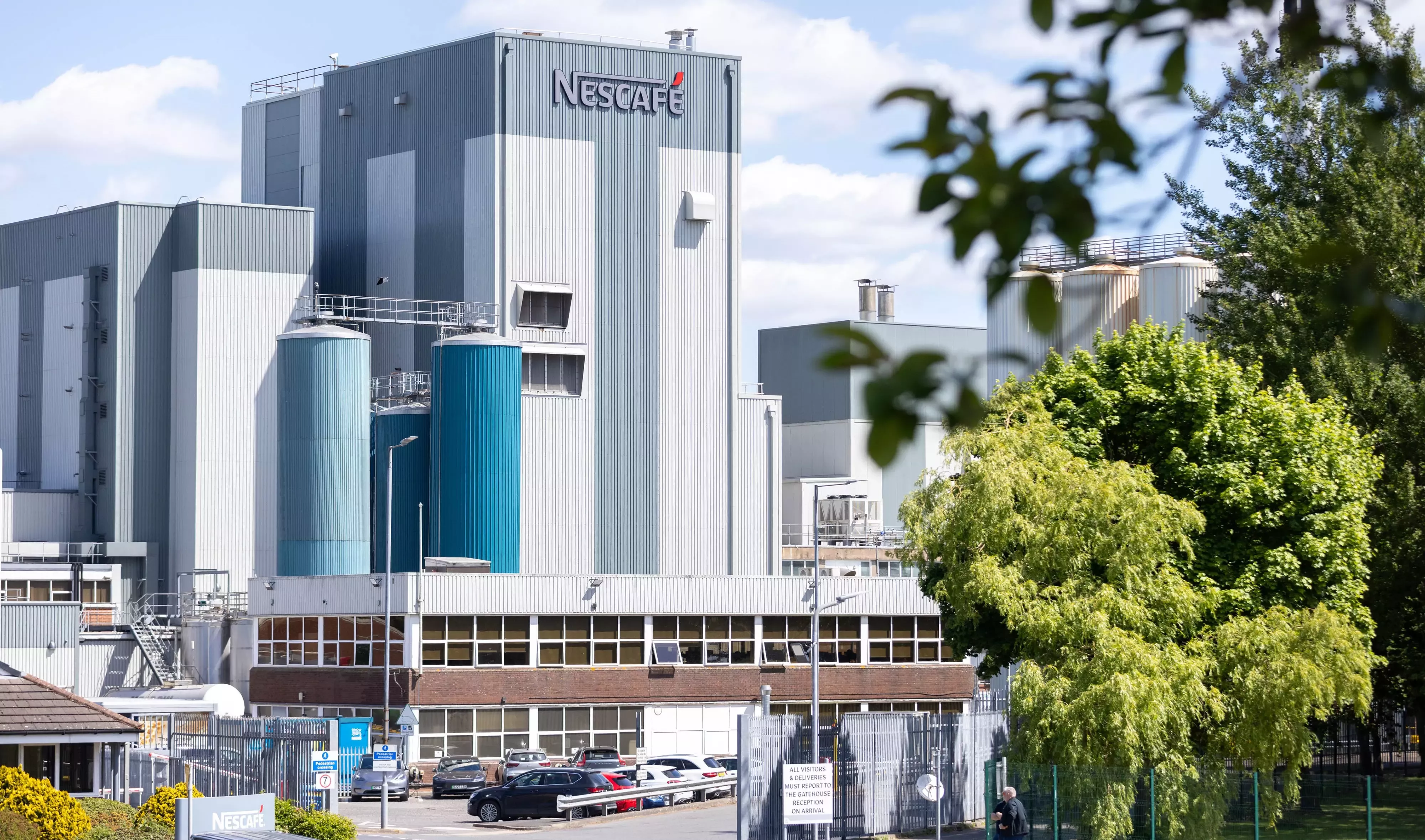 A landscape image of Dalston coffee factory, with lush green trees in the foreground and a Nescafé sign visible.