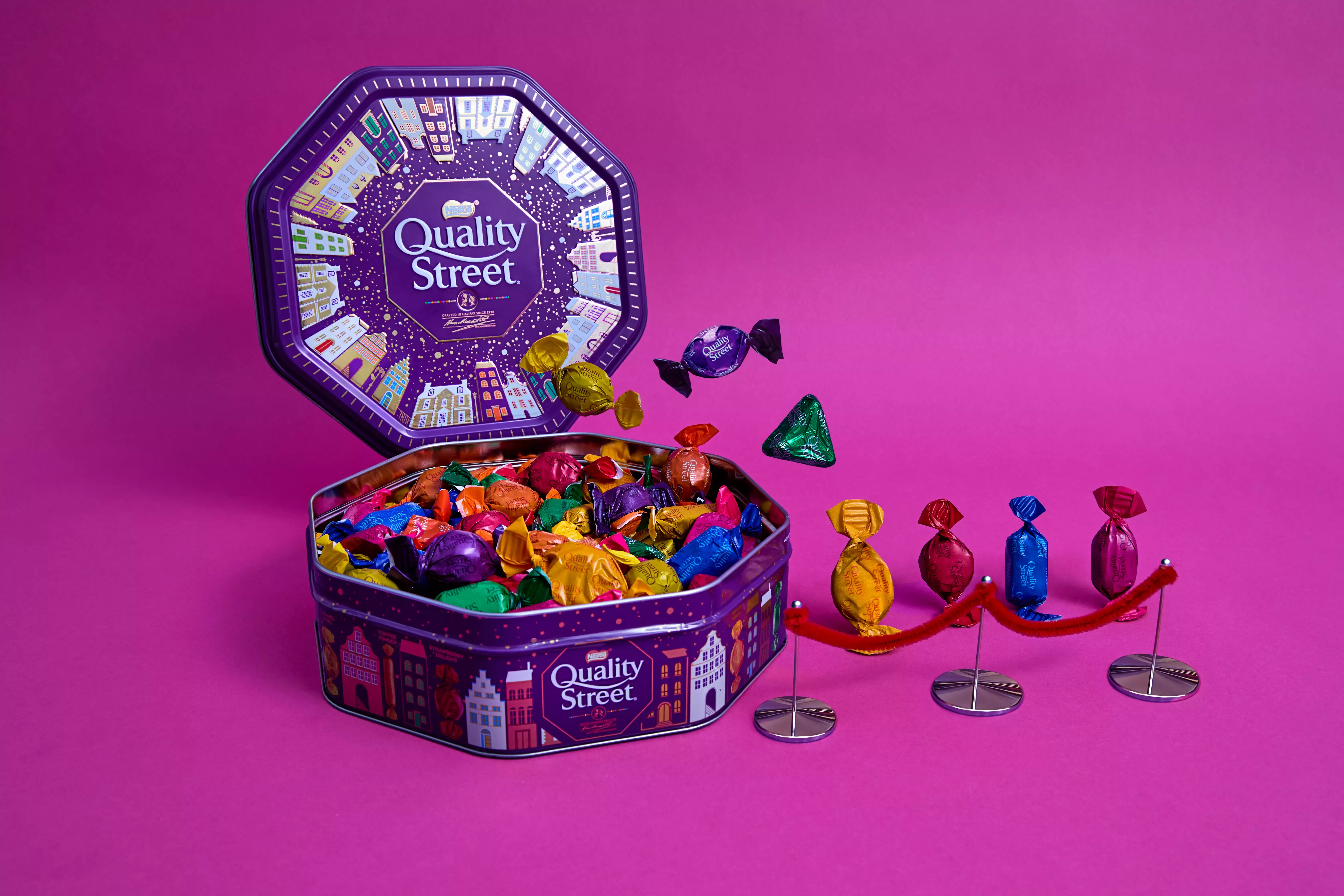 Quality Street tin with sweets in and other sweets lining up to get in