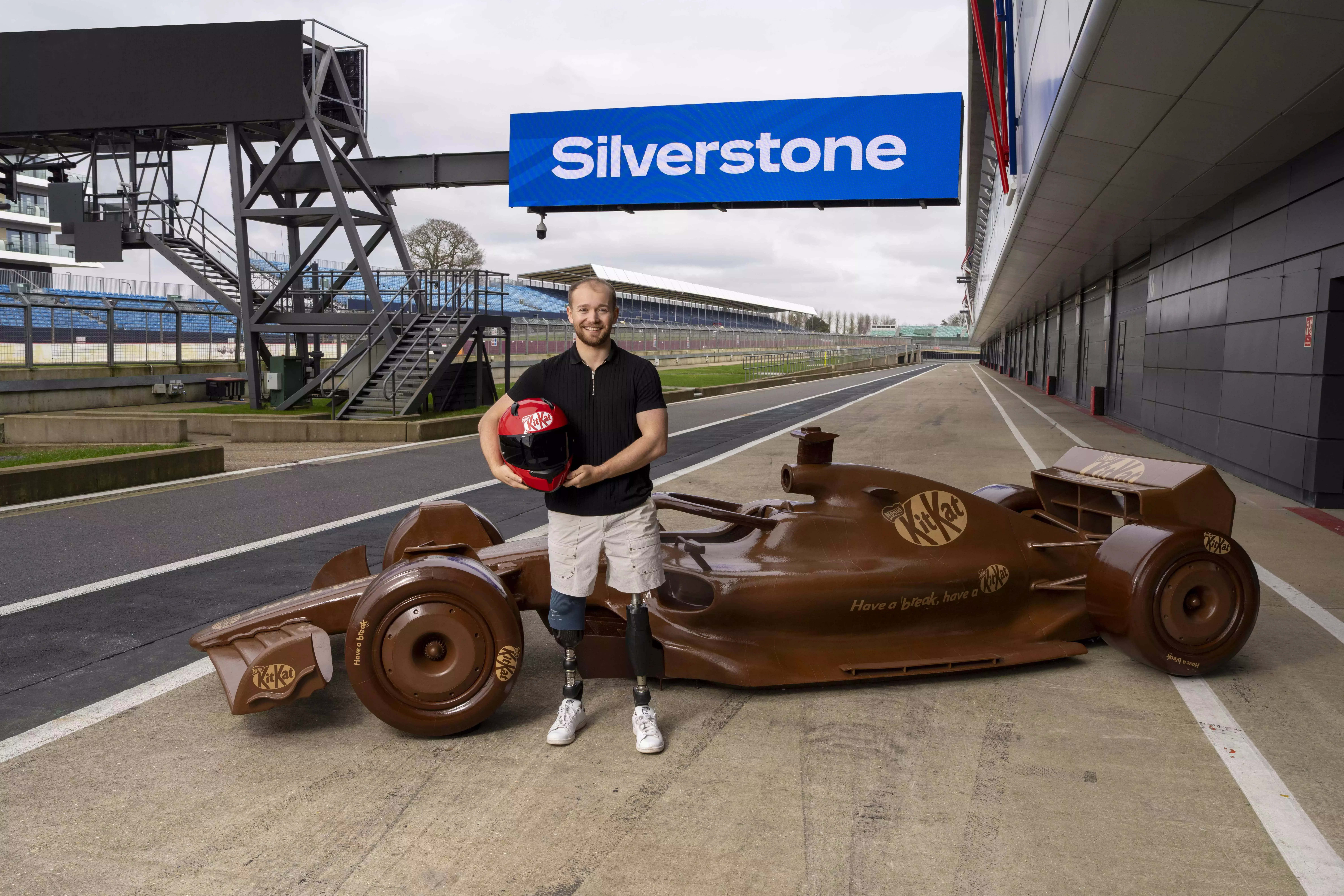 Billy Monger standing in front of KitKat F1 chocolate car at Silverstone