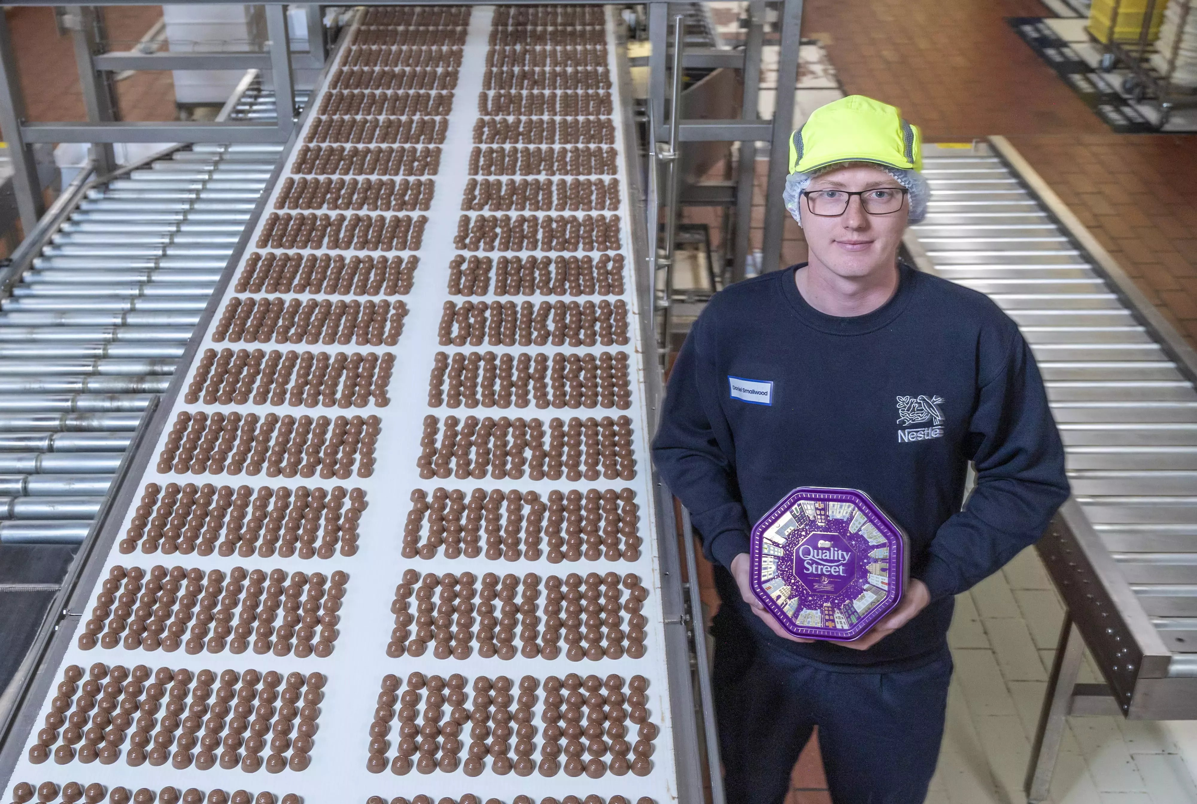 Man holding Quality Street tin standing next to production line