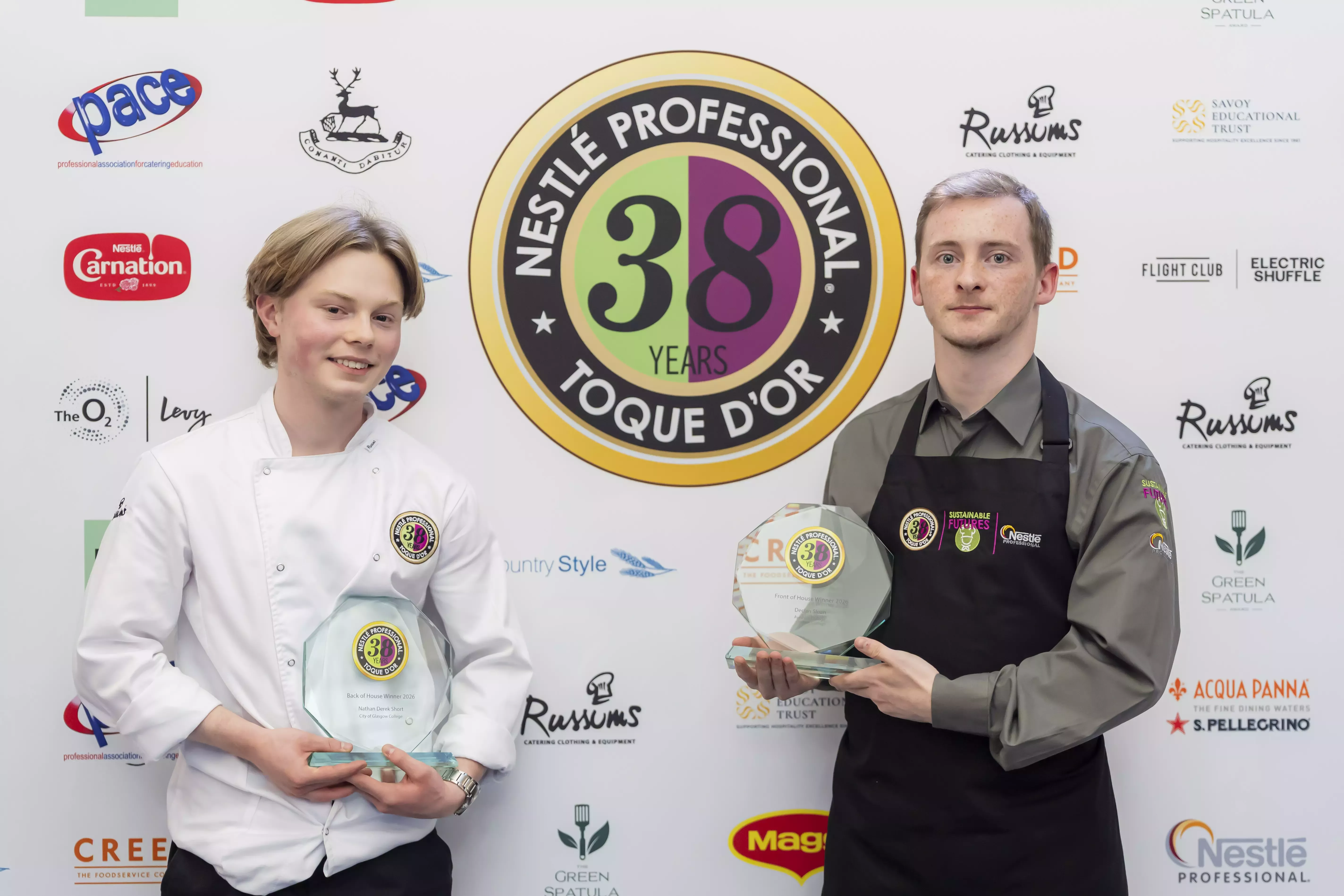 Two winners holding glass awards in front of a Nestlé Professional Toque d'Or branded wall.