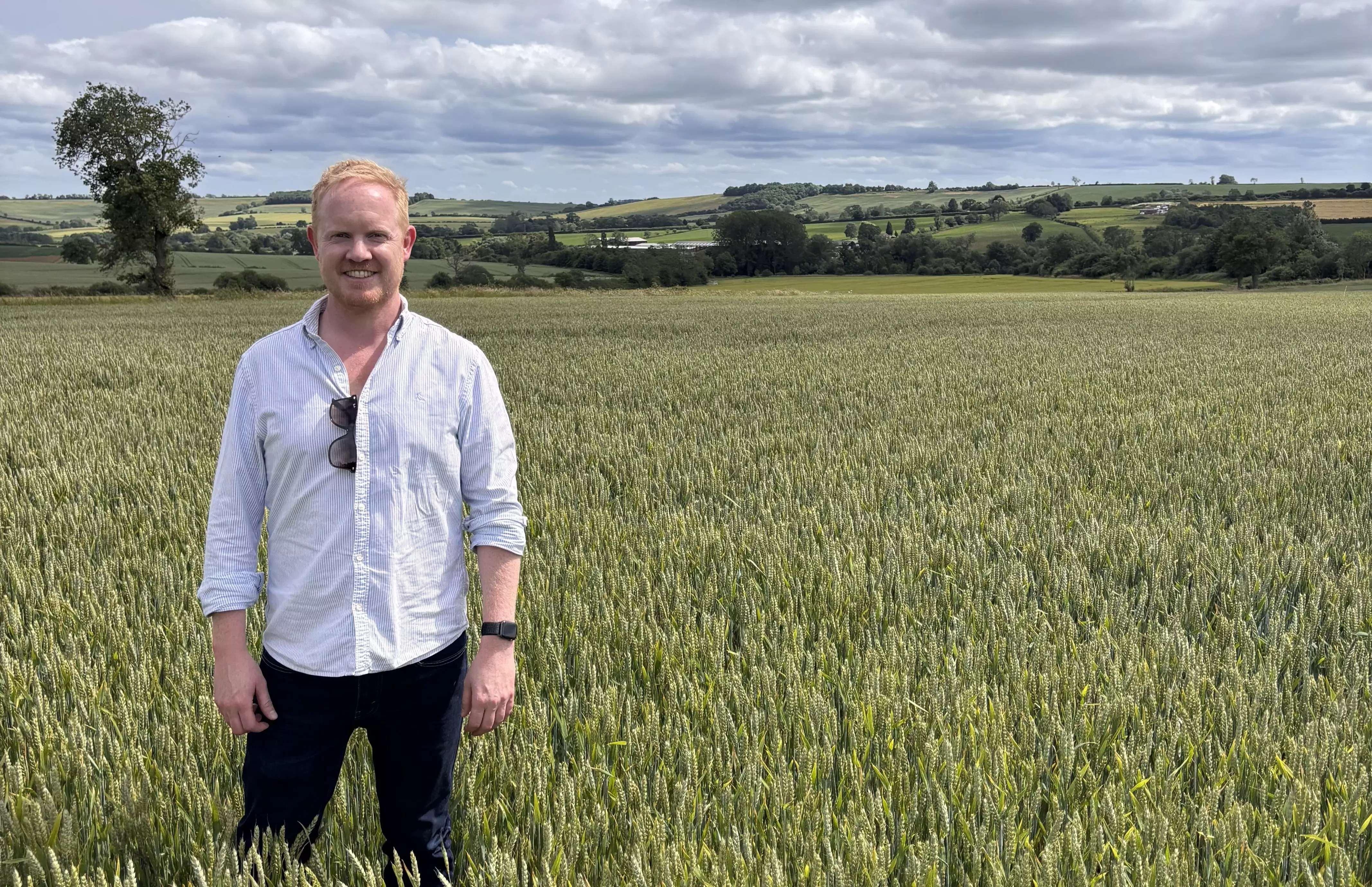 Man in white shirt and dark trousers standing in a field on a farm environment.