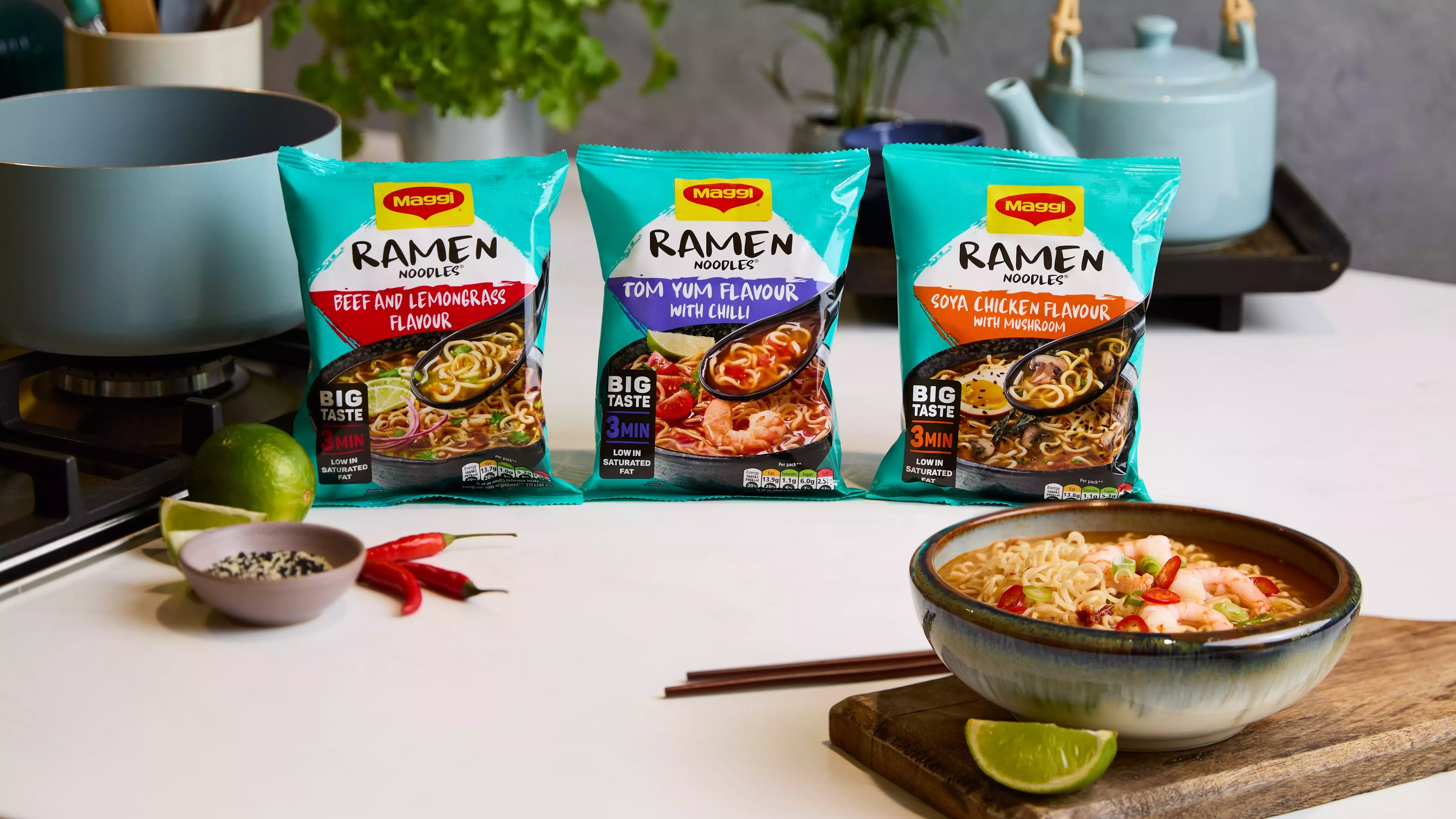 Kitchen worktop with three packets of new Maggi Ramen Flavours behind a bowl of noodles and various ingredients.