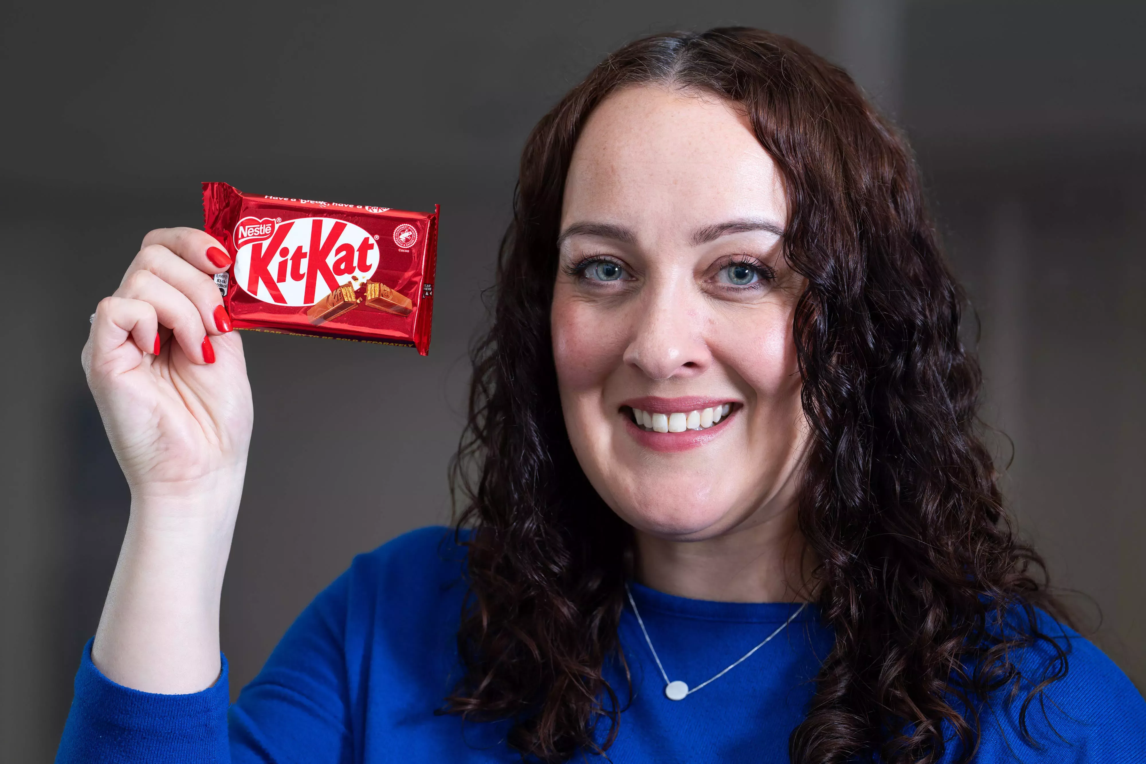 Woman wearing a blue top holding up a KitKat bar next to her head.