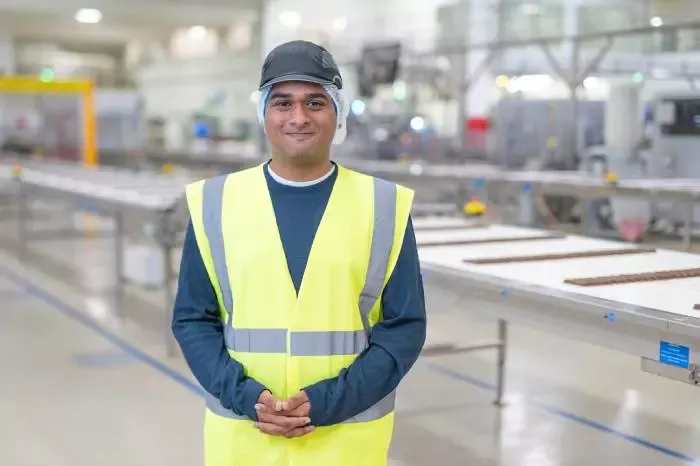 Person wearing high-visibility clothing standing in a manufacturing facility beside a production line.
