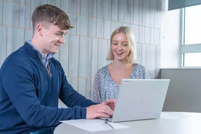 Two people working together on a laptop in an office.