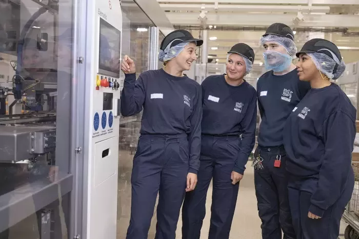 Four people standing beside machinery in a production facility